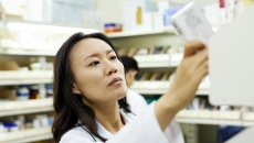 Pharmacist in a pharmacy looking at a piece of paper while holding it up to the light Pharmacist in a pharmacy looking at a piece of paper while holding it up to the light