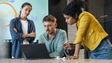 Three people in an office standing around a computer
