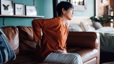 Person sitting on a couch while holding their back and their stomach