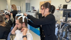 A therapist-in-training putting on the SynPhNe device on a volunteer's head A therapist-in-training putting on the SynPhNe device on a volunteer's head