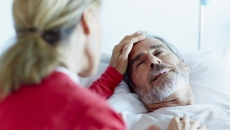 Person in a red shirt sitting next to someone in a hospital gown lying in a bed Person in a red shirt sitting next to someone in a hospital gown lying in a bed