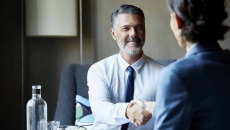 Two people sitting across from each other at a desk shaking hands Two people sitting across from each other at a desk shaking hands