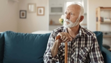 Person sitting on a couch looking away from the camera while holding a wooden cane Person sitting on a couch looking away from the camera while holding a wooden cane
