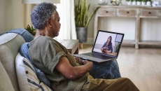 Person sitting on their couch in their home while talking to a telehealth provider on their computer Person sitting on their couch in their home while talking to a telehealth provider on their computer