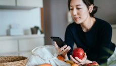 Person leaning against a counter holding an apple while looking at their phone Person leaning against a counter holding an apple while looking at their phone