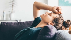 Person lying on a couch with their hand on their forehead with their eyes closed Person lying on a couch with their hand on their forehead with their eyes closed