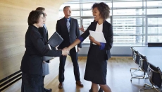 Four business people standing in a room with two of them shaking hands Four business people standing in a room with two of them shaking hands