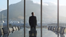 Person standing by a large window with their back turned looking at a large mountain Person standing by a large window with their back turned looking at a large mountain