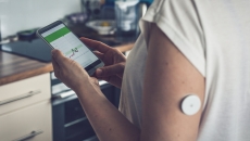 A person wearing a CGM patch checking their blood glucose level on a mobile app A person wearing a CGM patch checking their blood glucose level on a mobile app
