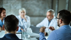 Group of people, two in lab coats, sit around table Group of people, two in lab coats, sit around table