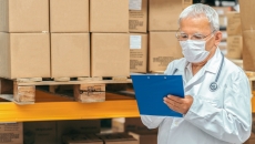Healthcare provider looking at a document with boxes behind them Healthcare provider looking at a document with boxes behind them
