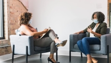 Two people seated, wearing masks Two people seated, wearing masks