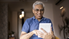 Person in a blue shirt holding a tablet while smiling and looking at the device Person in a blue shirt holding a tablet while smiling and looking at the device