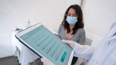 Person holding tablet in front of person wearing surigical mask Person holding tablet in front of person wearing surgical mask