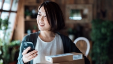 Person standing in their living room holding a phone and standing by stacked boxes Person standing in their living room holding a phone and standing by stacked boxes
