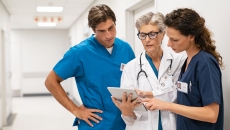 Healthcare providers standing in the hallway of a hospital looking at a tablet Healthcare providers standing in the hallway of a hospital looking at a tablet