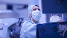 Healthcare provider wearing scrubs and a face mask while looking at a computer screen