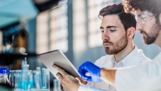 Two scientists in a laboratory setting looking at a tablet while surrounded by beakers Two scientists in a laboratory setting looking at a tablet while surrounded by beakers
