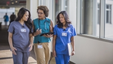 Three healthcare providers walking through a hall while looking at a tablet Three healthcare providers walking through a hall while looking at a tablet
