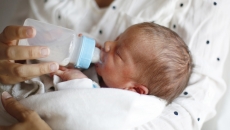 Person holding another small person while feeding them with a bottle Person holding another small person while feeding them with a bottle