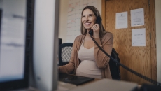 Pregnant person sitting at a desk talking on the phone while looking at a computer Pregnant person sitting at a desk talking on the phone while looking at a computer