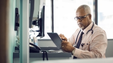 Healthcare provider sitting at a desk and looking at a tablet Healthcare provider sitting at a desk and looking at a tablet