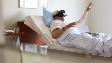 Person in a clinical setting lying in bed with their hand raised while wearing a virtual reality headset Person in a clinical setting lying in bed with their hand raised while wearing a virtual reality headset