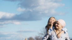 Person wearing a scarf on their head holding a child on their back with the sky behind them Person wearing a scarf on their head holding a child on their back with the sky behind them