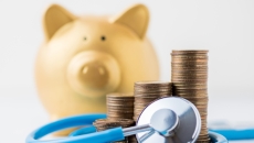 A piggy bank next to a stethoscope and a pile of coins A piggy bank next to a stethoscope and a pile of coins