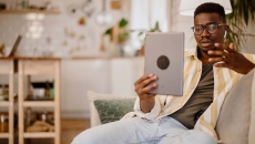 Person sitting on the couch in a home while holding up a tablet in front of them Person sitting on the couch in a home while holding up a tablet in front of them