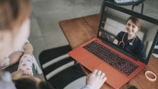 Two individuals sitting on a couch looking at a computer that is on a coffee table with a healthcare professional on the screen Two individuals sitting on a couch looking at a computer that is on a coffee table with a healthcare professional on the screen
