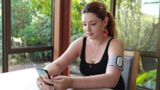 A person wearing an armband with the Theranica device while holding a smartphone. A person wearing an armband with the Theranica device while holding a smartphone.