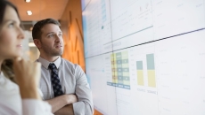 Two businesspeople looking at charts displayed on a large screen Two businesspeople looking at charts displayed on a large screen