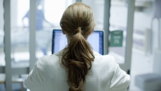 Woman doctor with long red hair using laptop in hospital, photographed from behind Woman doctor with long red hair using laptop in hospital, photographed from behind