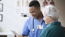A doctor and a patient look at a tablet in his office. A doctor and a patient look at a tablet in his office.