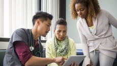 A doctor using a tablet while talking to a patient and her family member. A doctor using a tablet while talking to a patient and her family member.