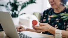 Person holding a prescription bottle while using a laptop Person holding a prescription bottle while using a laptop