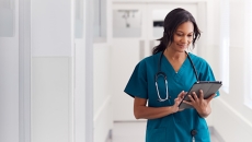 Healthcare provider wearing scrubs with a stethoscope around their neck while walking down the hallway of a health center Healthcare provider wearing scrubs with a stethoscope around their neck while walking down the hallway of a health center