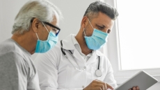 Patient and doctor in masks looking at tablet