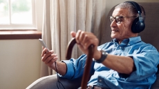 An older man wearing headphones and using a smartphone in his home An older man wearing headphones and using a smartphone in his home