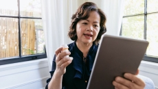 An older woman holding a pill bottle talking to a provider using her tablet. An older woman holding a pill bottle talking to a provider using her tablet.