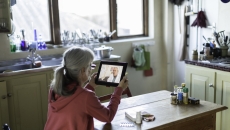 A woman using a tablet to talk to a provider at her kitchen table