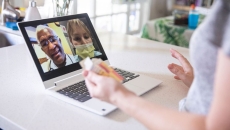 A close up of a woman holding a pill bottle while talking to two providers on her laptop. A close up of a woman holding a pill bottle while talking to two providers on her laptop.