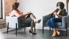 While wearing protective face coverings, a therapy patient and therapist discuss something. While wearing protective face coverings, a therapy patient and therapist discuss something.