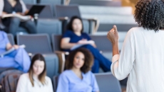 Several people sitting in a classroom with a teacher with their back faced to the camera