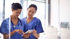 Two healthcare professionals standing next to each other while looking at a tablet