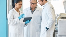 Three healthcare professionals standing in a circle looking at a tablet