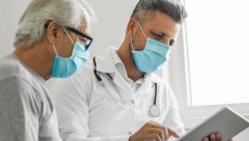 Healthcare provider sitting with a patient while looking at a tablet