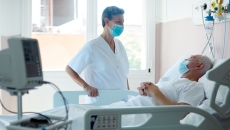 Person in mask standing over person in hospital bed Person in mask standing over person in hospital bed