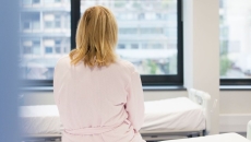 A person sitting on a hospital bed with her back to the camera. A person sitting on a hospital bed with her back to the camera.